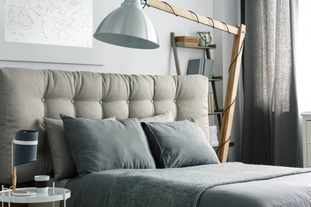 Grey bed with quilted headboard and big wooden lamp